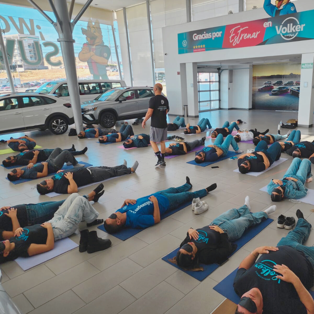 Grupo de colaboradores en empresa automotriz participando en breathwork empresarial para trabajo en equipo, productividad y bienestar laboral